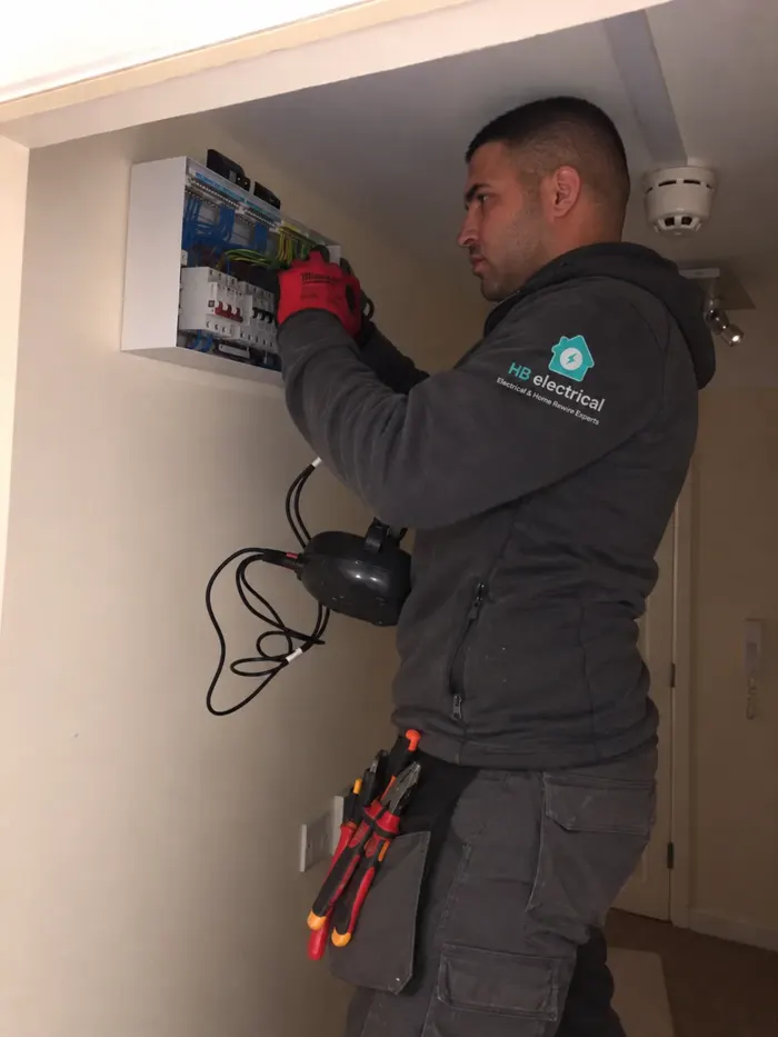 HB Electrical electrician in a branded hoodie testing at a consumer unit with a multifunction tester