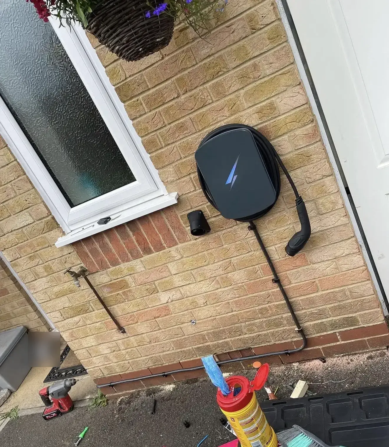 Dark wall-mounted EV charger beside a window on yellow brick