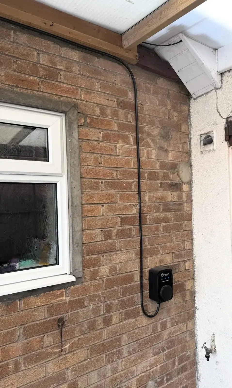 EV charger on a brick wall under a canopy with the cable routed up the wall